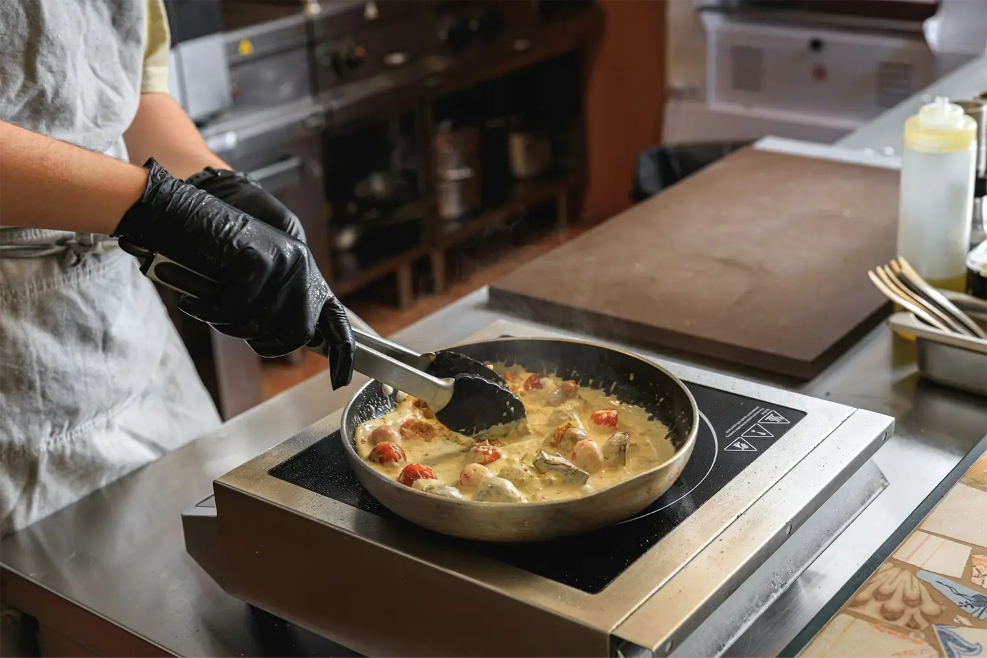 Close up of chef in uniform is cooking dish on frying pan for client order