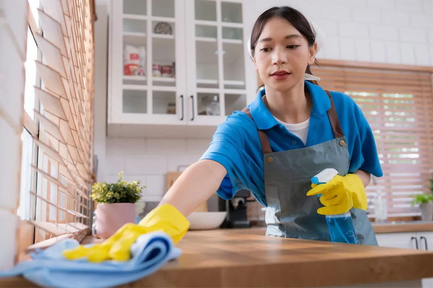 Cleaning service. Close-up of woman in apron and rubber gloves cleaning wooden table with spray