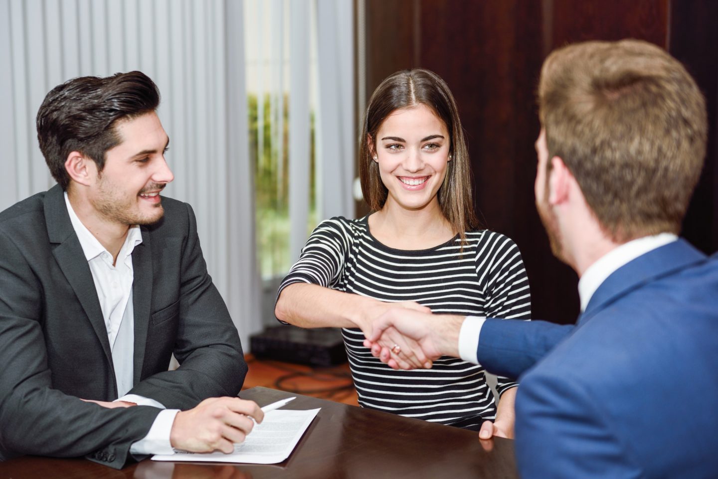 Smiling young couple shaking hands with an insurance agent