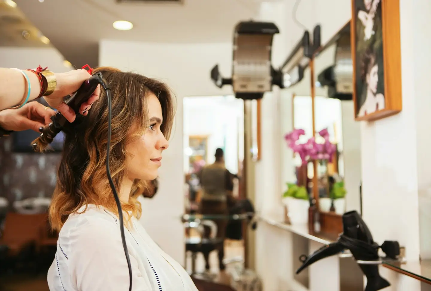 Hairdresser using curling tongs on customer's long brown hair in salon