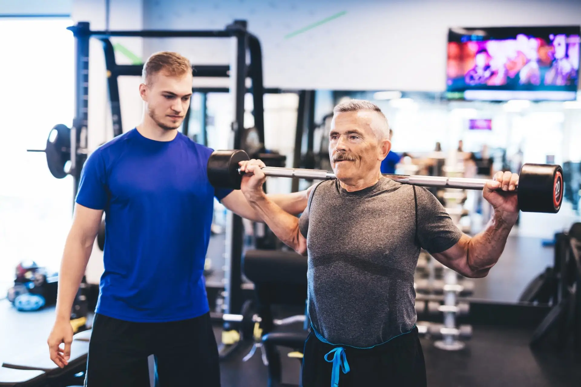 older-man-assisting-senior-man-at-the-gym-e1677564441929